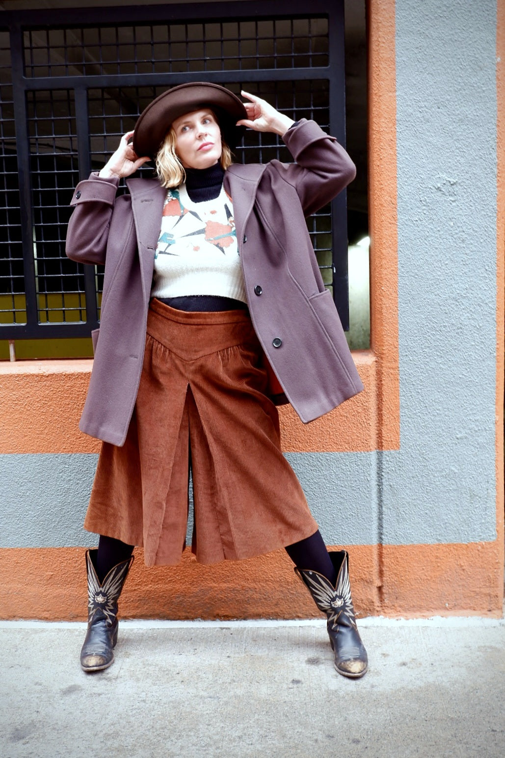 Model adjusting a brown felt hat while wearing an oversized mauve wool coat