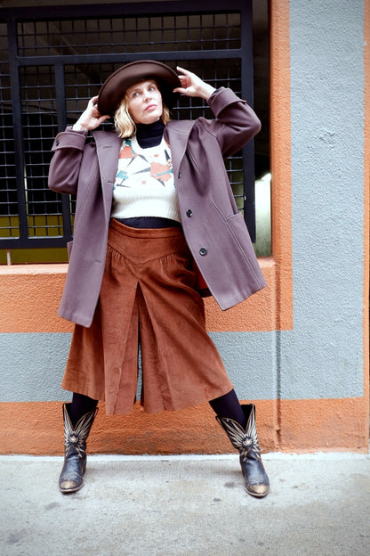 Model adjusting a brown felt hat while wearing an oversized mauve wool coat