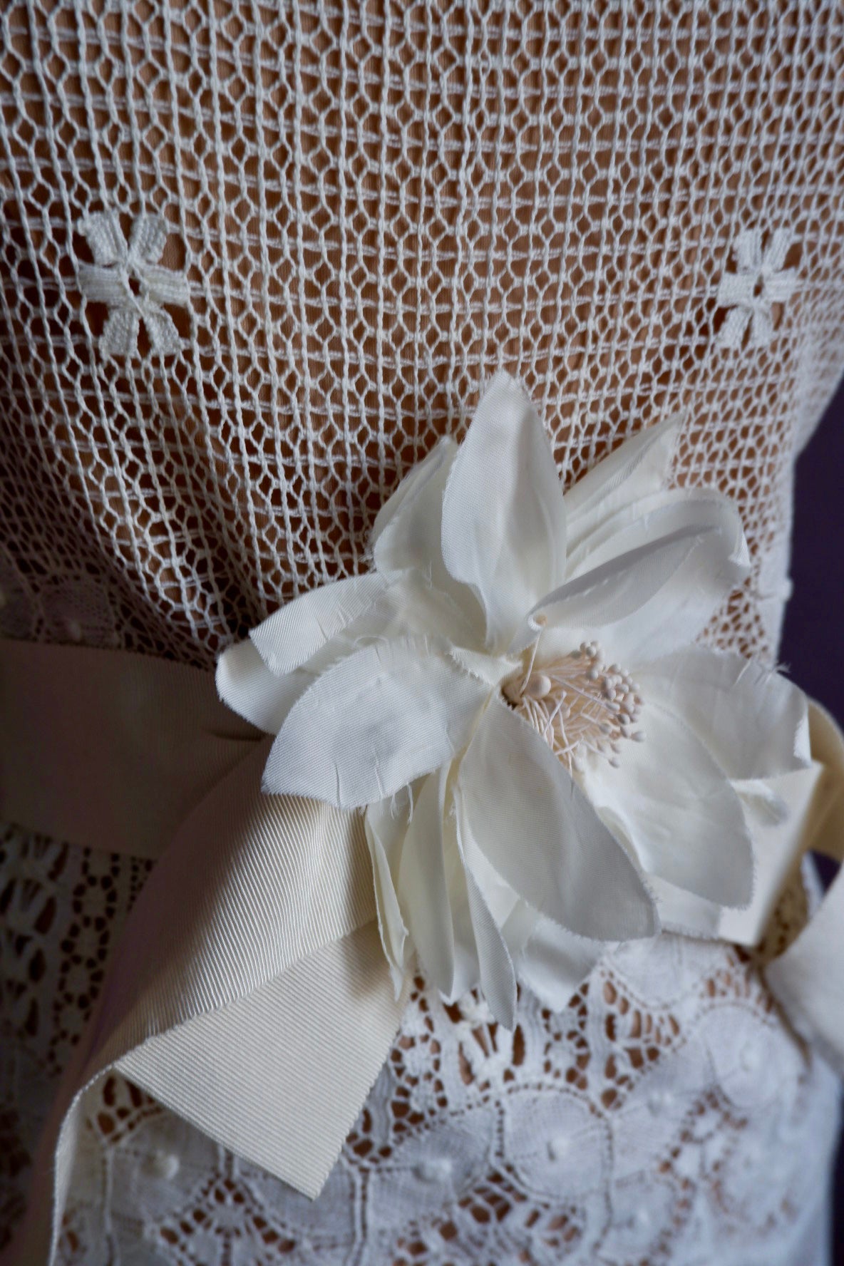Close-up of ivory silk flower with stamen center on grosgrain sash over netted lace