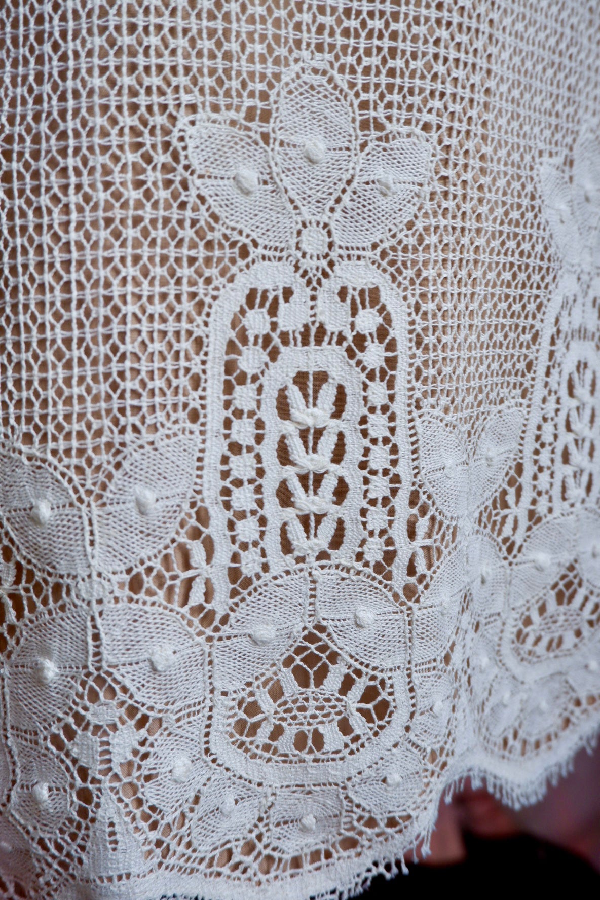 Detail of heavy ivory lace border with raised dots and scalloped lash edge on skirt hem