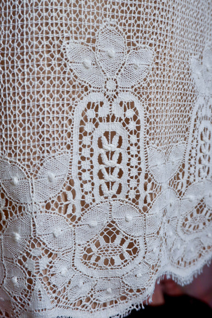 Detail of heavy ivory lace border with raised dots and scalloped lash edge on skirt hem