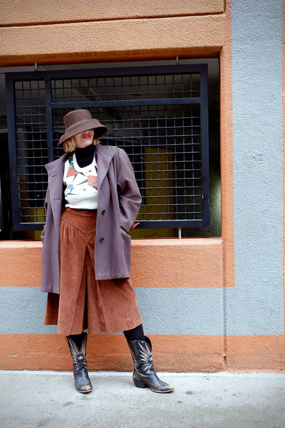 Model in a cream Pandora dancing-couple sweater vest layered under a mauve coat