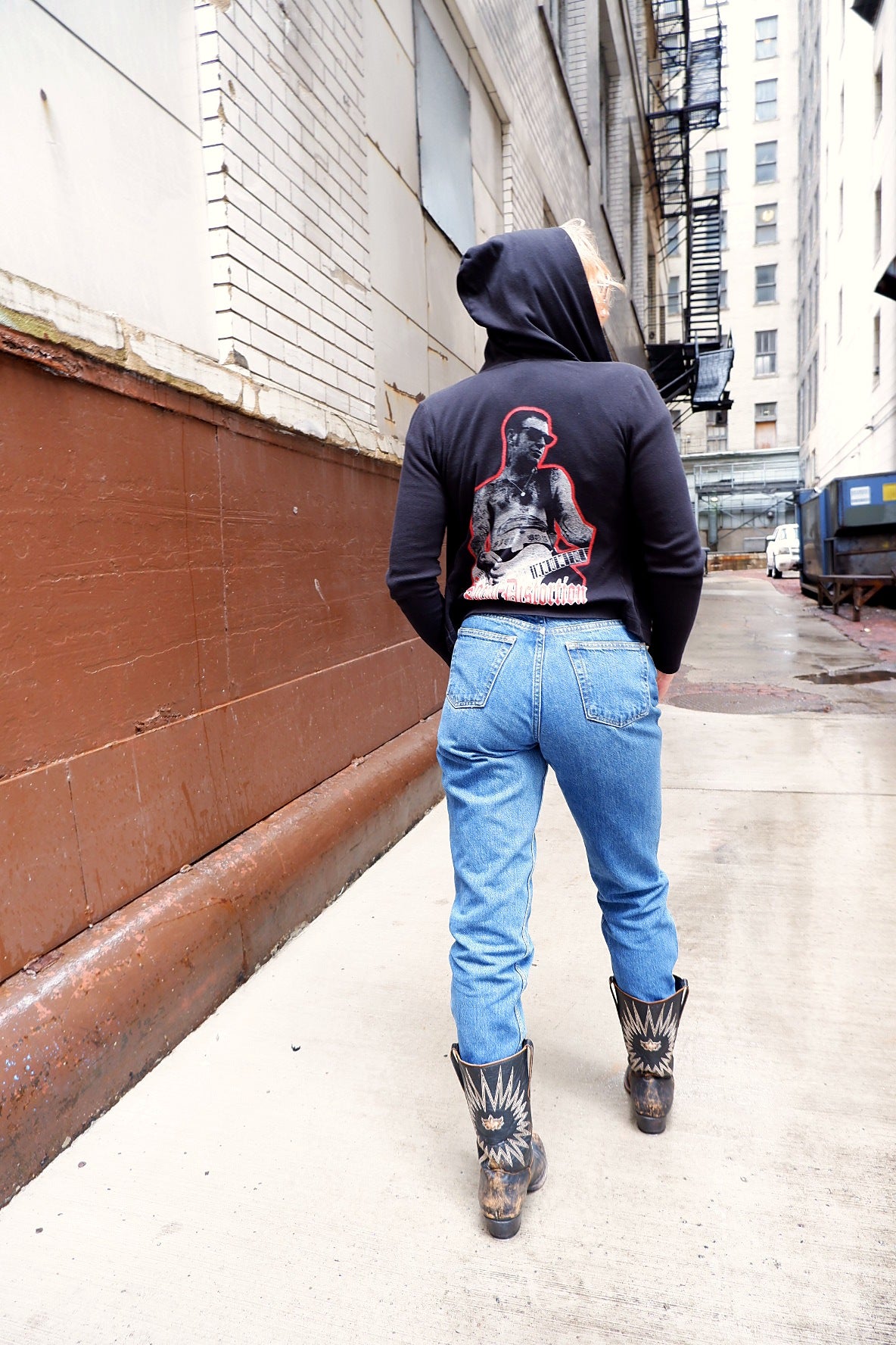 Full-length back view of a Social Distortion hoodie with the hood up in a downtown alley