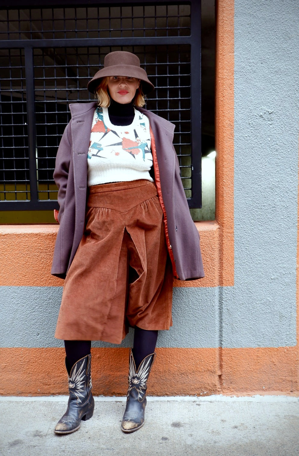 Model in a 1980s Brittany oversized mauve wool coat over rust corduroy culottes and cowboy boots