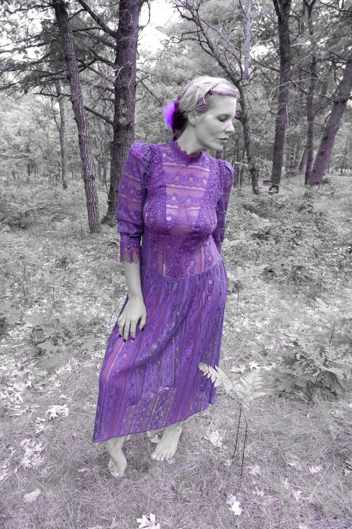 Model looking down in a plum lace maxi dress in the woods (artistic color edit)