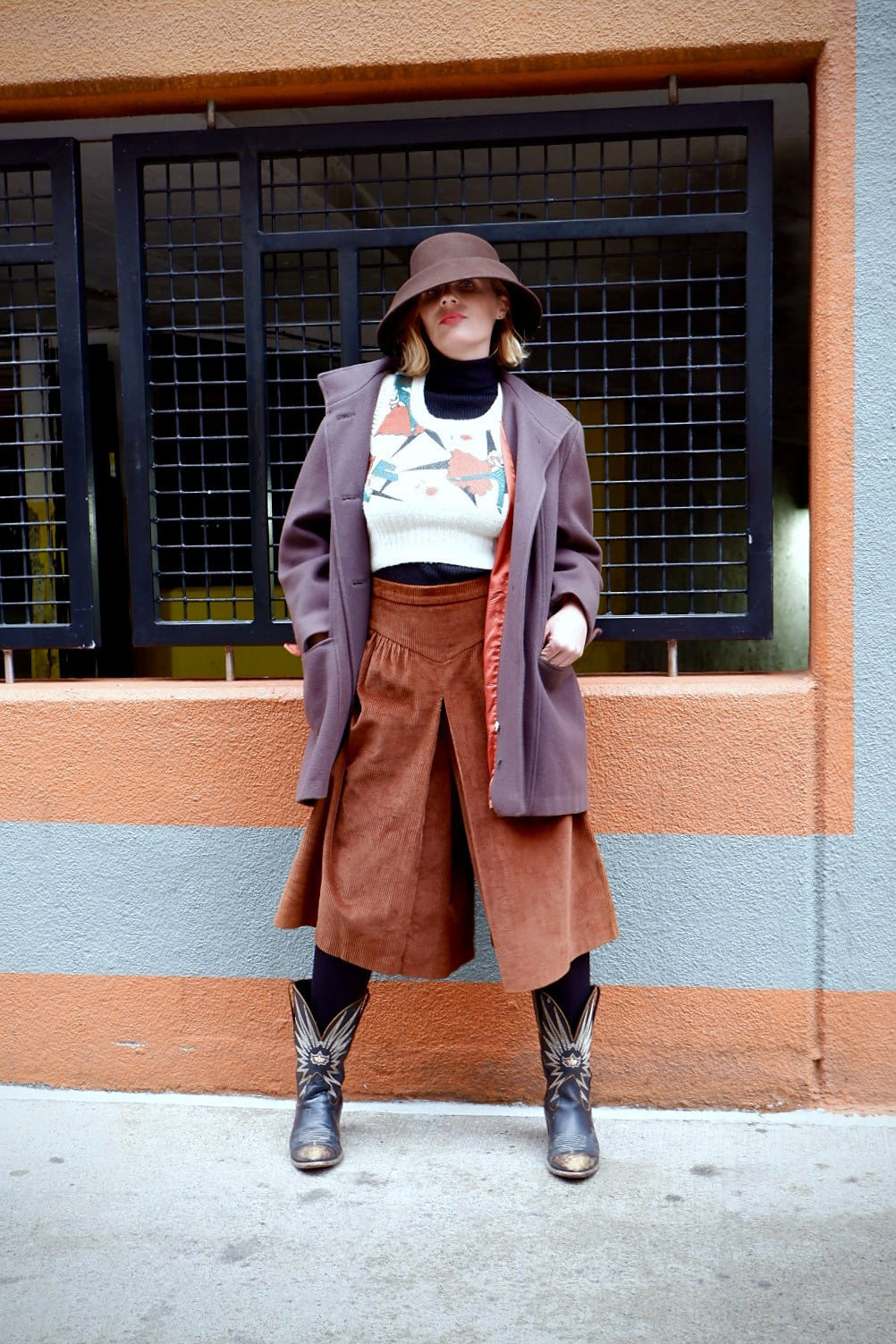 Model in a sculptural brown wool felt hat with a mauve wool coat and rust corduroy culottes