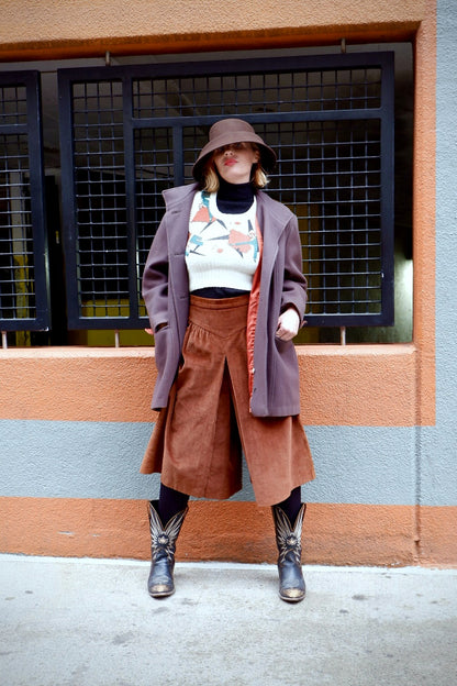 Model in a sculptural brown wool felt hat with a mauve wool coat and rust corduroy culottes