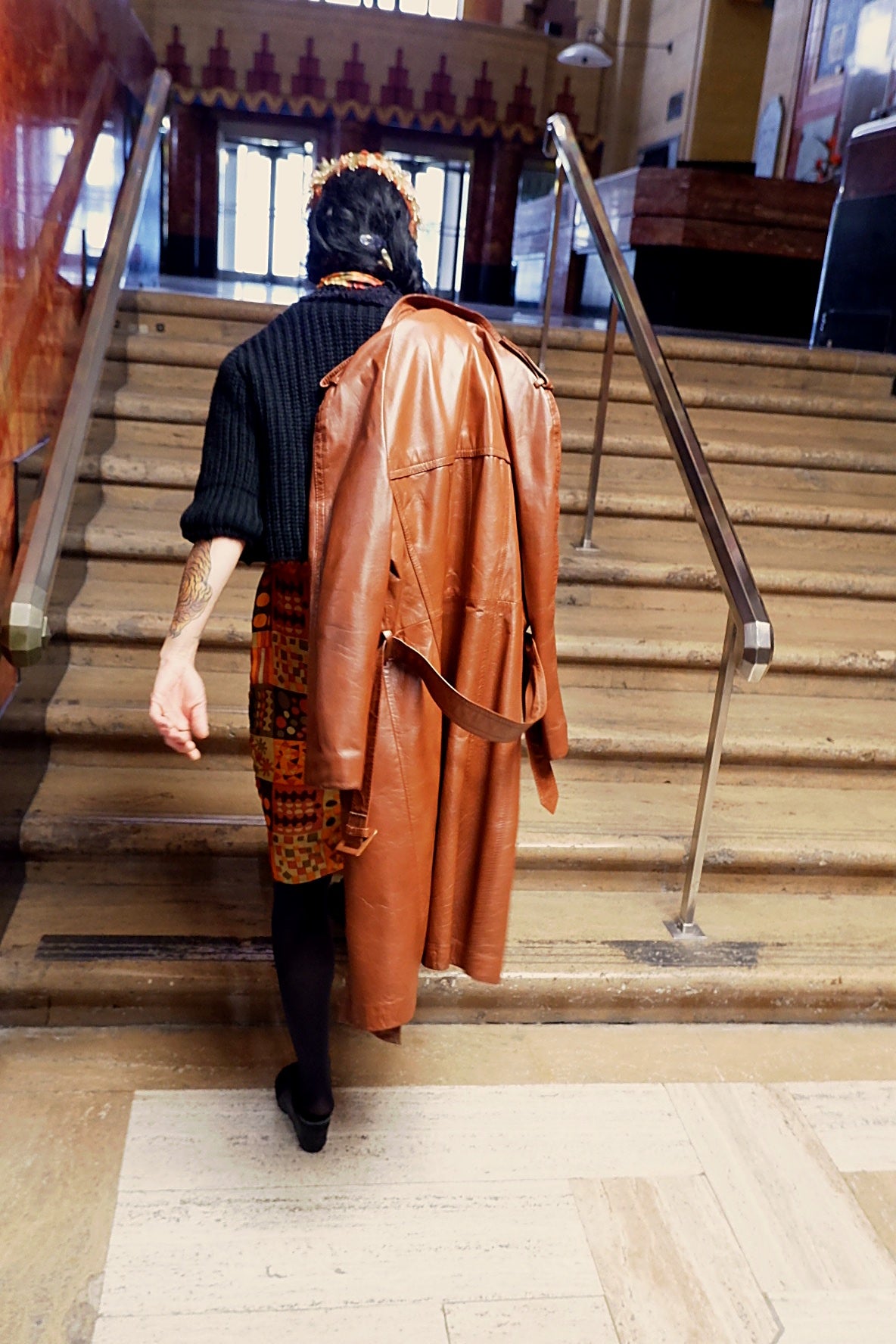 Cognac leather trench coat draped over the shoulder on marble stairs