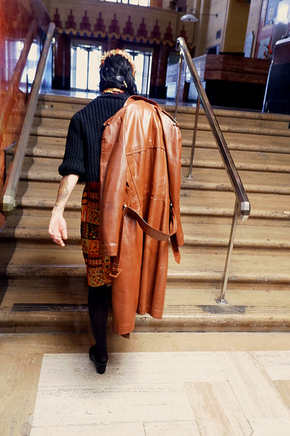 Cognac leather trench coat draped over the shoulder on marble stairs