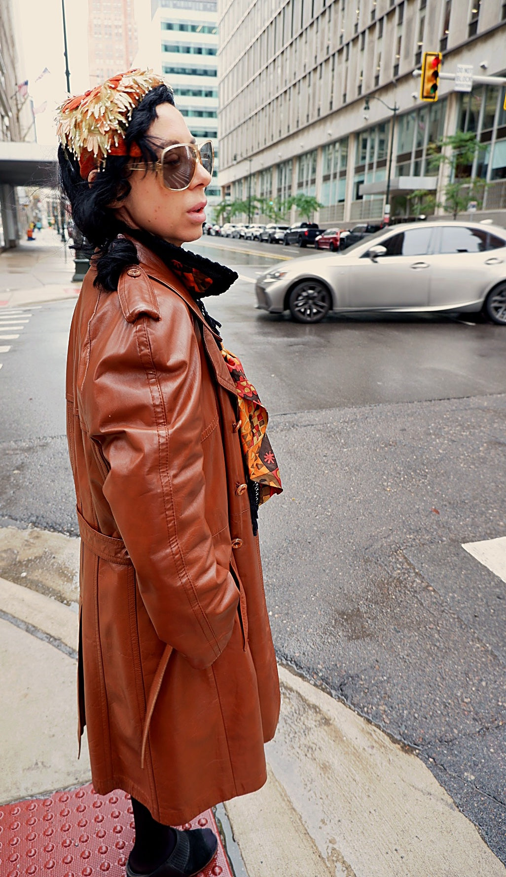 Side profile of a vintage cognac leather trench coat worn on a city street corner