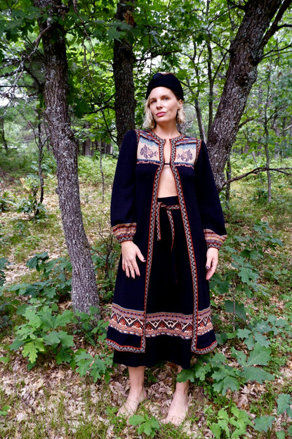Model in a 1970s John Ashpool knit duster, skirt and belt set standing in a forest