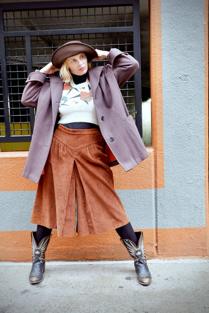 Model in rust corduroy wide-leg culottes with box pleat, cowboy boots and a mauve wool coat
