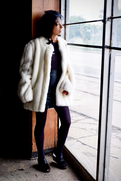 Model in an ivory faux fur coat looking out a tall warehouse window