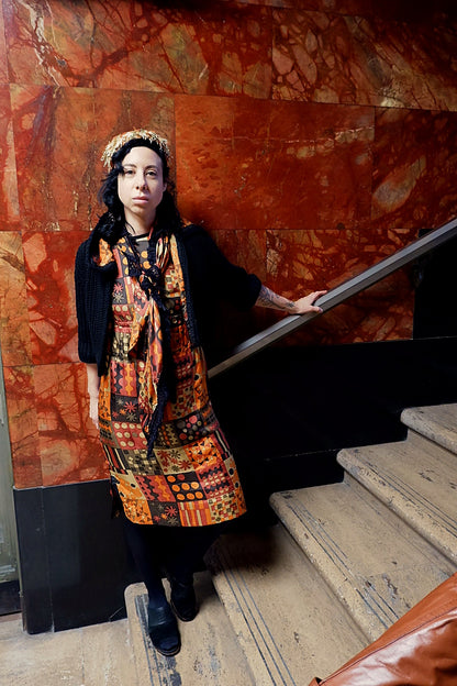 Handmade vintage mod print dress set with black knit sweater and fringed piano shawl against red marble