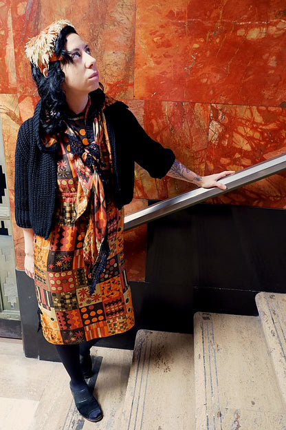 Model looking up in a handmade mod geometric print dress, reversible knit sweater and fringed shawl
