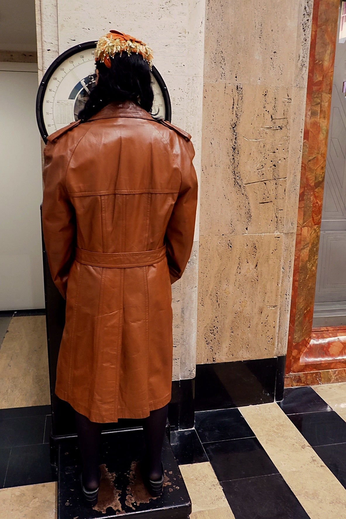 Three-quarter view of cognac leather trench coat with epaulettes, storm flap and self-belt