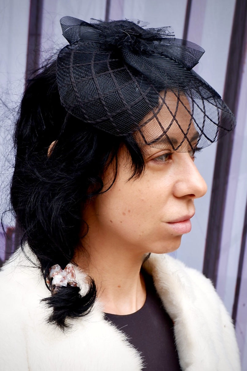 Close-up of a black fascinator headband with sculptural mesh bow and lattice birdcage veil