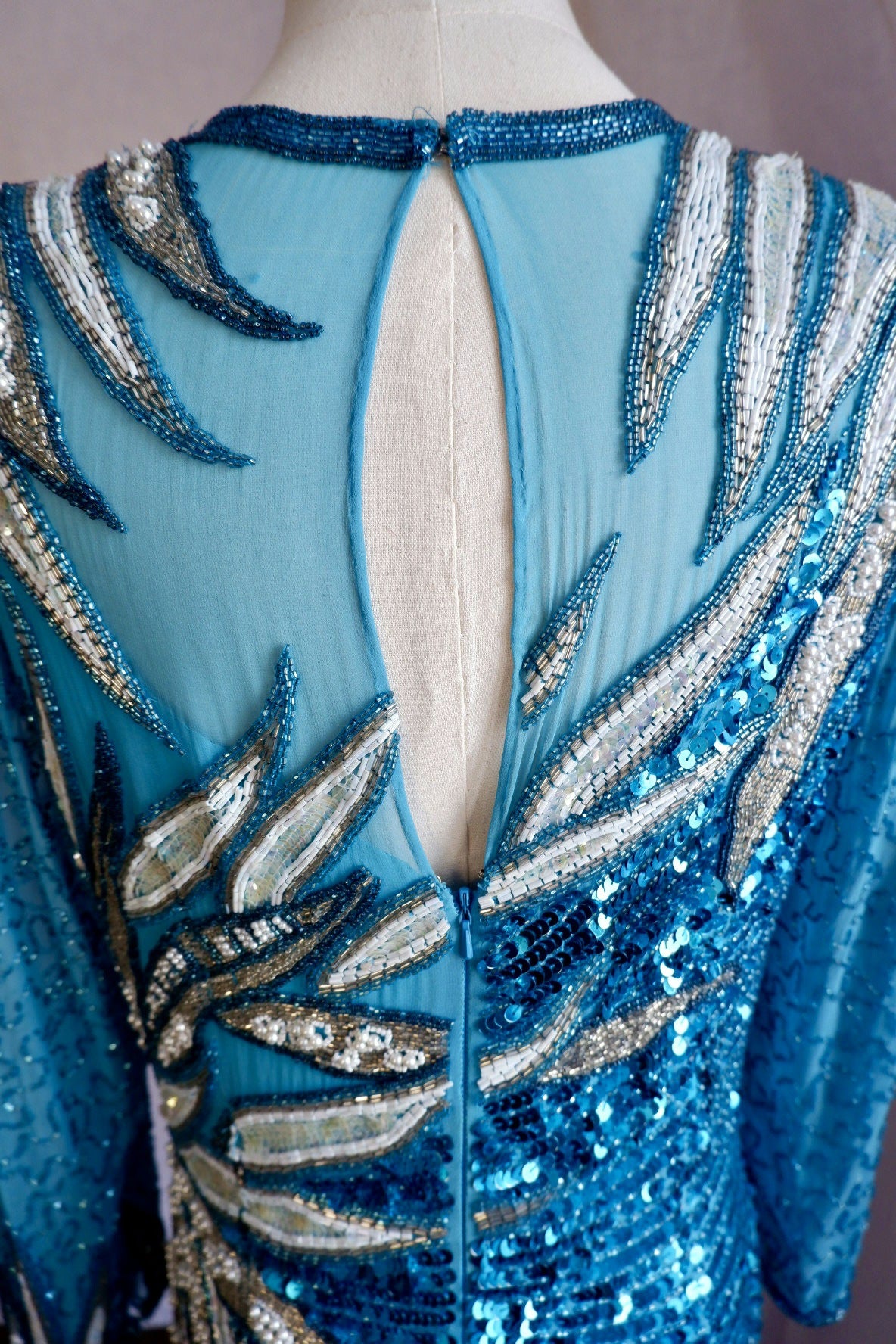 Back detail of hand-beaded gown showing sheer keyhole, zipper and white and silver bugle bead leaves