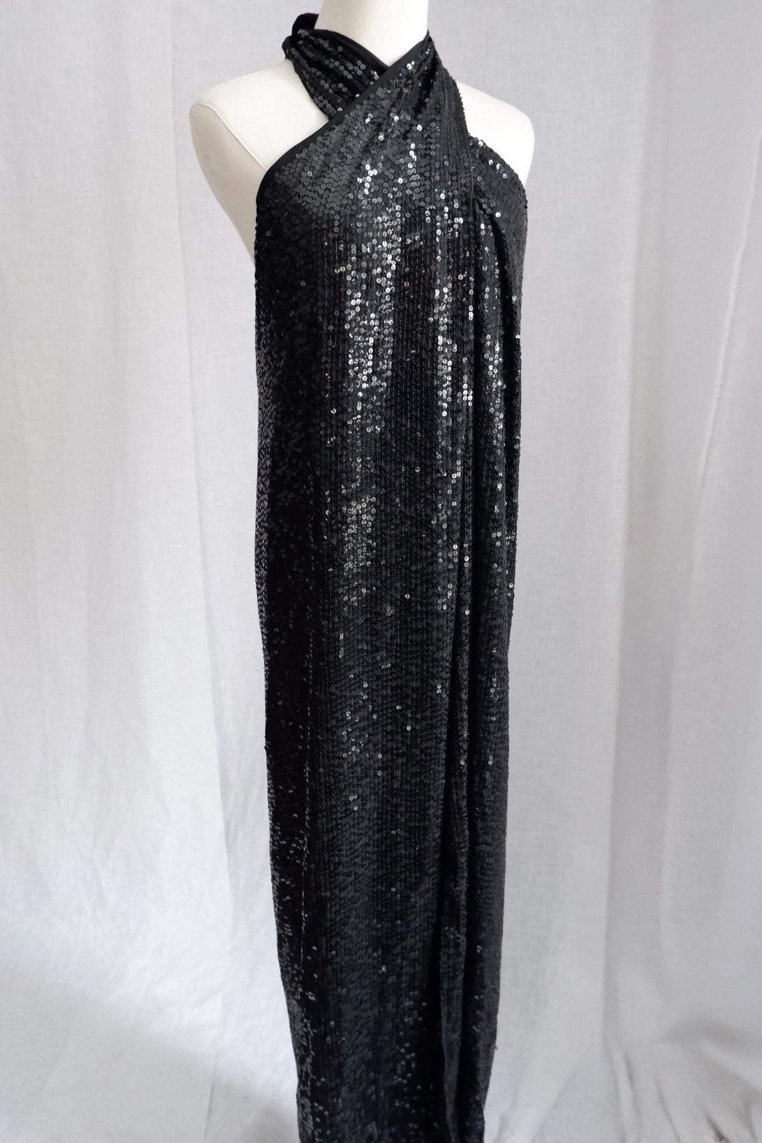 Angled front view of Donna Karan black sequin column gown with crossover halter neckline