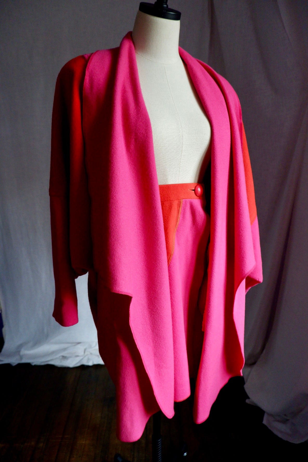 Angled view of Merle Chicago pink wool coat with waterfall front over matching skirt on dress form